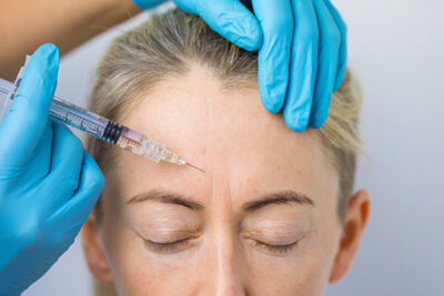 Doctor makes the rejuvenating facial injections for smoothing woman's forehead skin