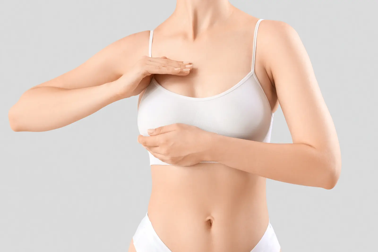 Woman in white bra examining breast for self-check.