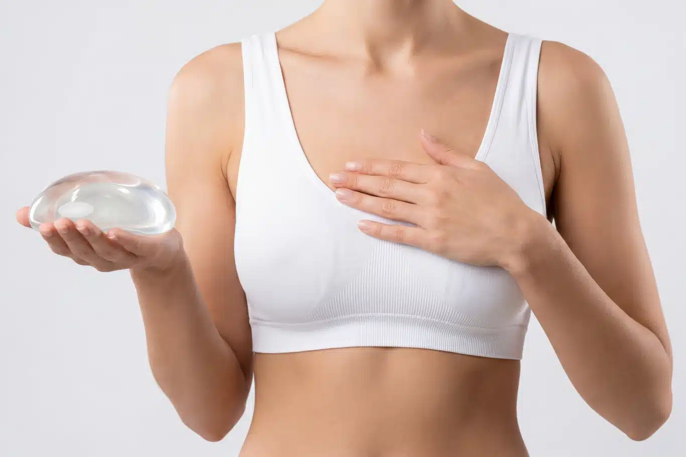 silicone implant natural feel Person holding breast implant, wearing a white sports bra.